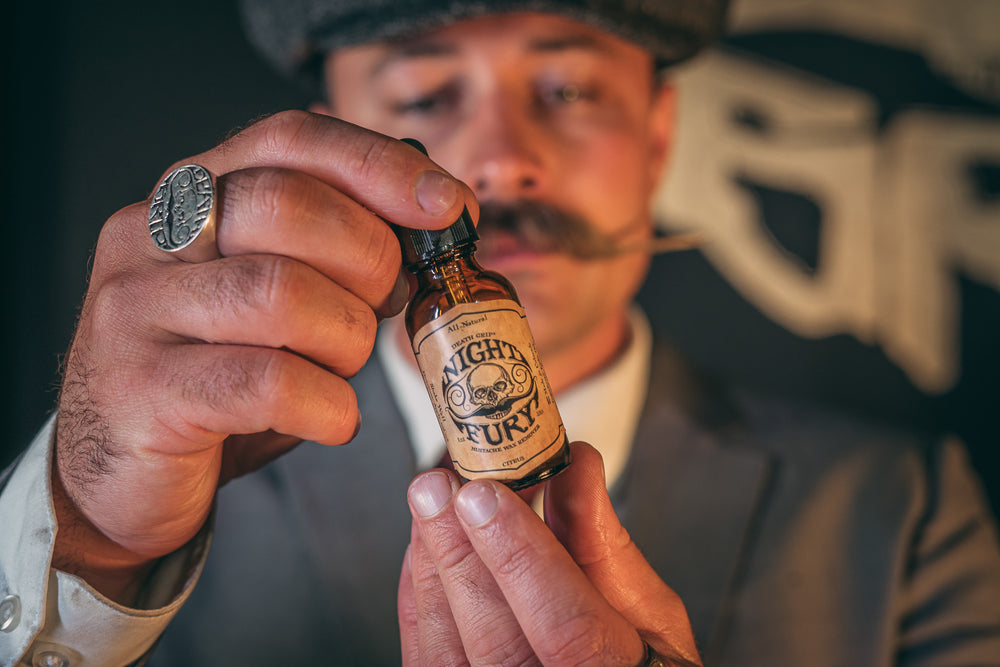 Man with mustache holding Night Fury mustache wax remover oil bottle in hand