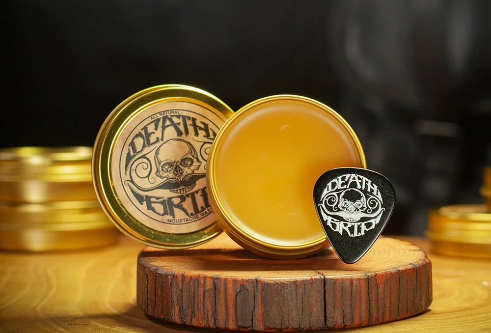 Death Grip mustache wax open tin with wax and branded pick on wooden stand with blurred tins in background