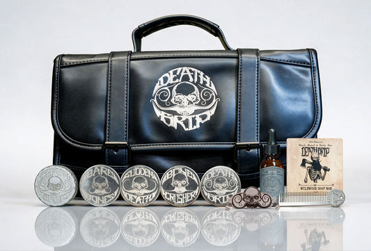 A black faux-leather messenger-style case with a silver Death Grip logo, displayed with multiple branded silver coin-like accessories, a small bottle, and a book on a light gray reflective studio background.